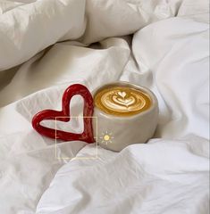 a cup of coffee sitting on top of a bed next to a heart shaped object