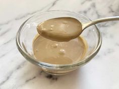 a spoon full of peanut butter sits in a glass bowl on a marble countertop