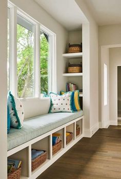 a window seat with pillows and books on it in front of a book shelf filled with books