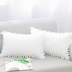 three white pillows sitting on top of a gray couch next to a book and flower