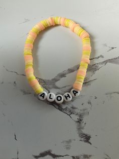 "this is a pink, bright yellow, and light yellow. clay beaded braclet made by me! It says \"aloha\" on it, Which means hello!" Colorful Beaded Yellow Bracelets For Vacation, Yellow Beaded Bracelet For Vacation, Yellow Bracelets With Round Beads For Vacation, Yellow Beaded Bracelets For Vacation, Pink Stretch Bracelet With Letter Beads For Vacation, Adjustable Yellow Friendship Bracelets With Letter Beads, Yellow Letter Beads Jewelry For Beach, Summer Yellow Bracelets With Letter Beads, Yellow Letter Beads Bracelets For Summer