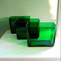 three green glass vases sitting on top of a white tableclothed countertop