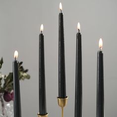 black candles with gold tips are lined up against a gray background in front of a floral arrangement