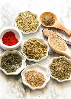 several bowls filled with different kinds of spices on top of a marble counter next to wooden spoons