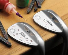 two golf wedges are sitting on a table next to some markers and pens,