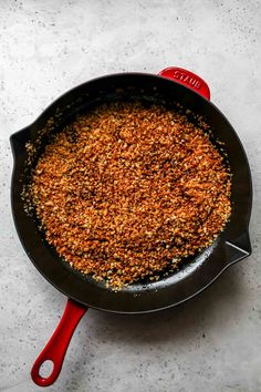 a frying pan filled with some food on top of a white counter next to a red spatula