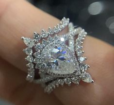 a woman's hand holding an engagement ring with a pear shaped diamond in the center