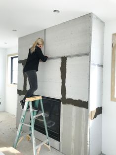 a woman standing on top of a step ladder in front of a fire place that is being built