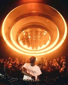 a dj is standing in front of a large circular light with his head turned to the side