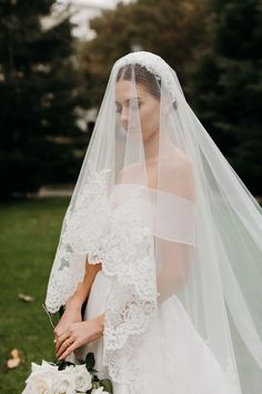 a woman wearing a wedding veil and holding a bouquet in her hand while standing on the grass