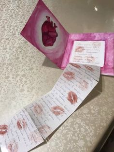 two folded cards with hearts on them sitting on a table next to a piece of paper