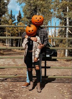 a man and woman are holding pumpkins on their heads while standing in front of a fence