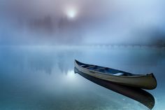 a boat floating on top of a lake under a foggy sky with trees in the background