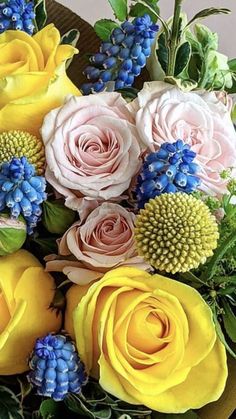 a bouquet of yellow and pink roses on a table with blue flowers in the center