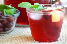 a glass filled with liquid next to a bowl full of cherries and mint leaves