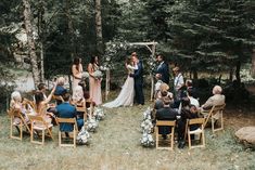 a wedding ceremony in the woods with people sitting on chairs and looking at each other