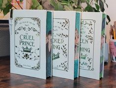 three books sitting on top of a wooden table next to a potted green plant