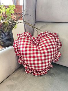 a heart shaped pillow sitting on top of a couch next to a potted plant