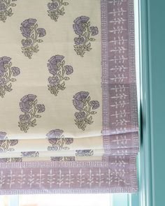 a purple and white flowered curtain hanging from a window