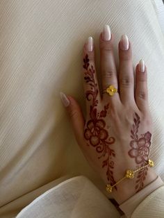 a woman's hand with henna and gold jewelry on her left arm, resting on a white couch