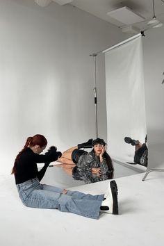 a woman sitting on the ground in front of a mirror with another person behind her