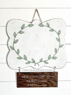 a wooden sign hanging on the side of a white wall with a green leaf wreath