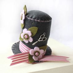 a gray hat with pink flowers and scissors on the top is sitting on a white surface