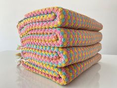 stack of multicolored crocheted towels on white table with white wall in background