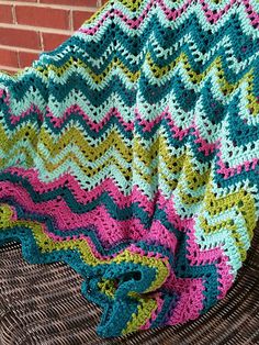 a crocheted blanket sitting on top of a chair next to a brick wall