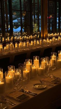 a long table with many lit candles and place settings on it in front of large windows