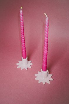 two pink candles with snowflakes on them sitting next to each other in front of a pink background