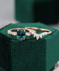 two gold rings with blue and white diamonds on top of a green velvet ring box