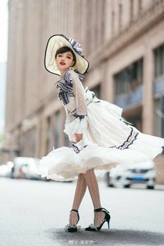 a woman in a white dress and hat is walking down the street