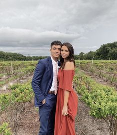 a man and woman in formal wear standing next to each other at an outdoor vineyard