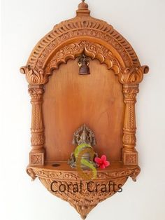 an ornate wooden wall mounted shelf with a bell on it's side and a red flower in the middle