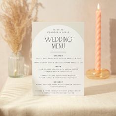 a wedding menu sitting on top of a table next to a candle