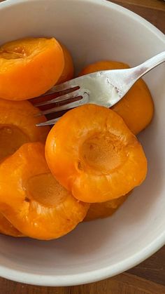 a white bowl filled with peeled apricots and a fork