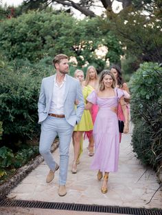 a group of people that are walking down a path together with one man in a suit and the other woman in a pink dress