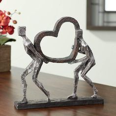 a sculpture of two people holding a heart on top of a wooden table