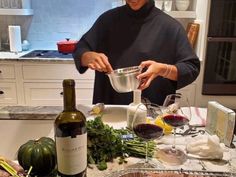 a woman pouring wine into a bowl on top of a counter next to vegetables and fruit