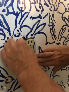 an older person is painting a wall with blue and white designs