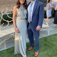 a man and woman standing next to each other in front of a white bench on grass