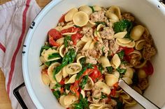 a white bowl filled with pasta, meat and veggies on top of a wooden table