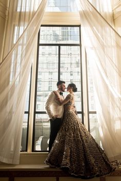 a bride and groom standing in front of a window with sheer curtains on the windowsill