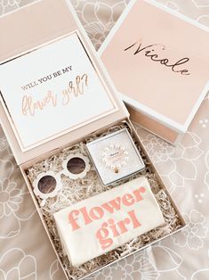 a flower girl gift box on a bed next to it's card and its contents