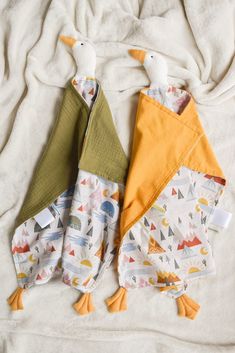 two baby bibs with ducks on them laying on a bed next to each other