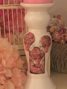 a white vase with pink flowers on the side and a candle in front of it