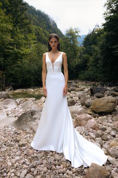 a woman in a white wedding dress standing on rocks next to a river and trees