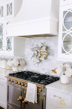 a kitchen with white cabinets and gold trim on the stove top, along with flowers in vases