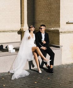 a man and woman sitting on a bench in front of a building with their legs crossed